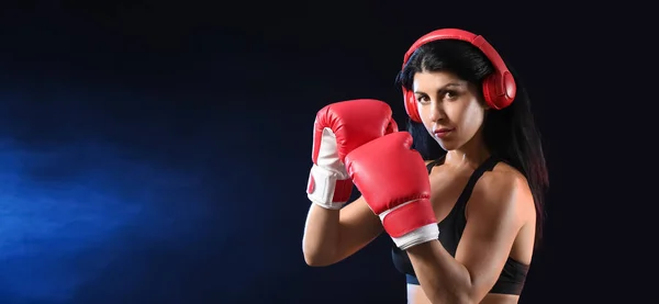 Sporty female boxer on dark background with space for text