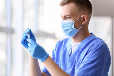 Hastanede şırıngalı tıbbi maskeli bir erkek doktor.