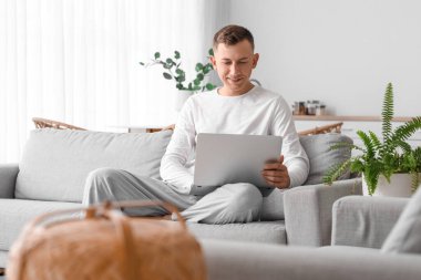 Evde kanepede dizüstü bilgisayar kullanan genç adam