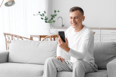 Cep telefonlu genç adam evdeki kanepede selfie çekiyor.