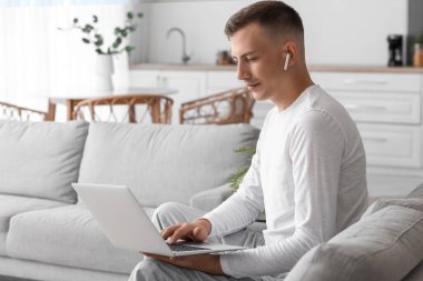 Evde kanepede dizüstü bilgisayar kullanan genç adam