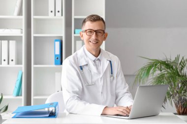 Klinikteki masada dizüstü bilgisayarla çalışan erkek doktor.