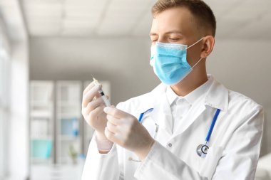 Tıbbi maskeli erkek doktor, hastanede şırıngalı, yakın plan.