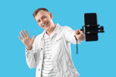 Cep telefonlu genç adam mavi arka planda selfie çekiyor.