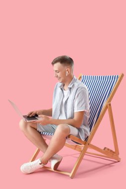 Genç adam pembe arka planda dizüstü bilgisayar kullanıyor.