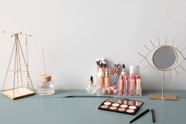 Dekoratif kozmetik, ayna, sazlık dağıtıcı ve aydınlık duvarın yanındaki masada takılara sahip organizatör