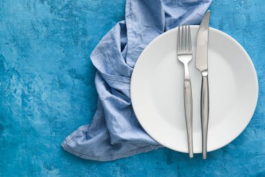 Tabakta çatal bıçak takımı ve mavi arka planda peçete ile basit masa ayarları