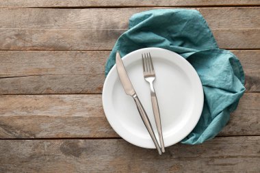 Beyaz tabakta çatal bıçak takımı ve tahta arka planda peçete.