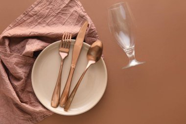 Tabakta çatal bıçak takımı, kahverengi arka planda peçete ve cam.