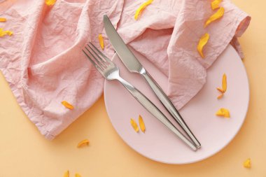 Sofra takımı, tabakta peçete ve sarı arka planda çiçek yaprakları.