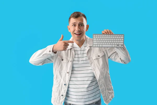 Surprised young man pointing at computer keyboard on blue background