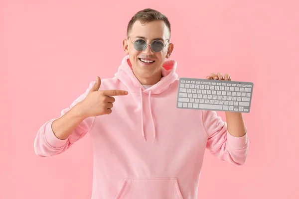 一个年轻人指着粉色背景的电脑键盘 — 图库照片