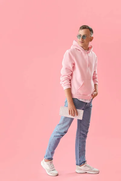 Young man with computer keyboard on pink background