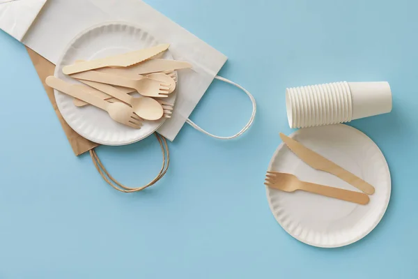 Eco tableware and paper bags on blue background