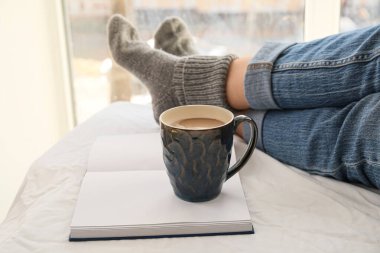 Kadın bacakları, kitap ve kahve pencerenin yanında.
