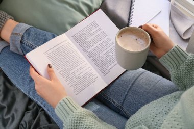 Woman with cup of coffee reading book, closeup
