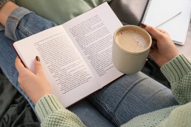 Woman with cup of coffee reading book, closeup