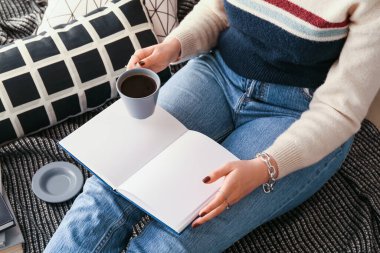 Woman with book and cup of coffee at home, closeup