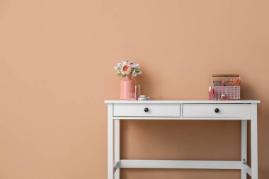 Çiçekli vazo, dekoratif kozmetik ürünleri ve renk duvarının yanındaki masada fırçalar.