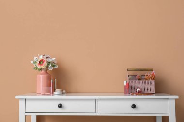 Çiçekli vazo ve renk duvarının yanındaki masada dekoratif kozmetik ürünleri düzenleyici.