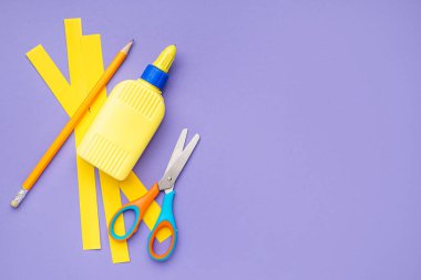 Renkli arka planda bir şişe tutkal, kağıt şeritler, kalem ve makas.