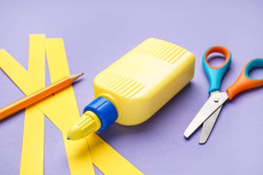 Renkli arka planda bir şişe tutkal, kağıt şeritler, kalem ve makas.