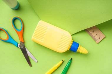 Yeşil arka planda bir şişe yapıştırıcı ve makas.