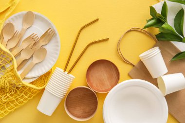 Sarı arka planda farklı çantalar, eko sofra takımı ve bitki dalı