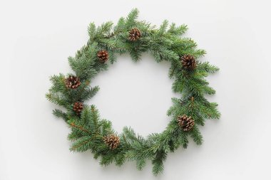 Beyaz arka planda köknar dalları ve çam kozalaklarından yapılmış Noel çelengi