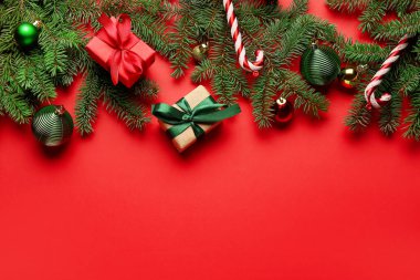 Kırmızı arkaplanda köknar dalları, Noel hediyeleri ve süslemeleri olan kompozisyon