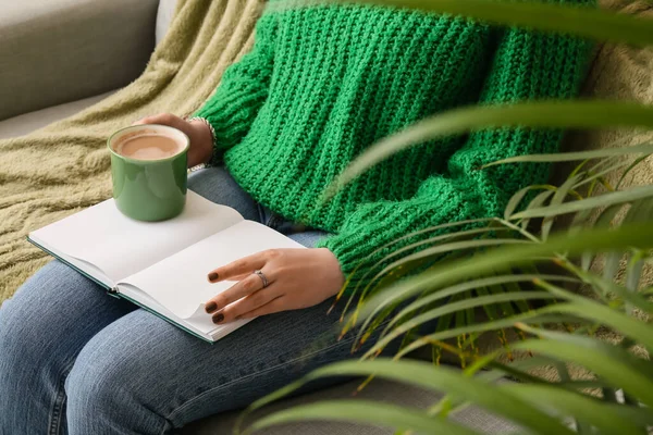 Woman with cup of coffee and book at home, closeup