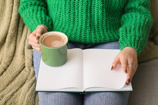 Woman with cup of coffee and book at home, closeup