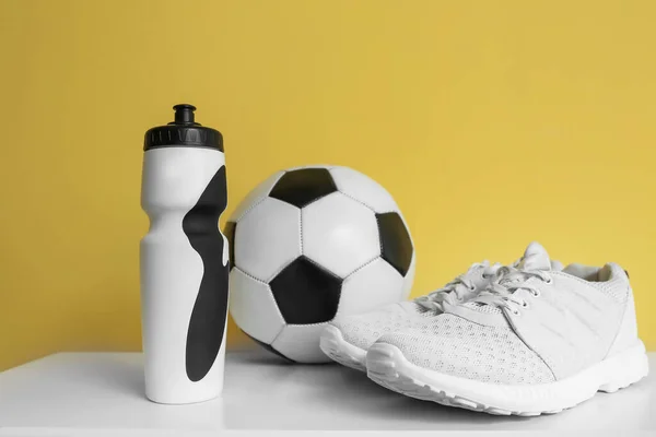 Bottle of water, soccer ball and sneakers on table near color wall