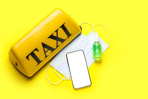 黄色の背景にタクシーの屋根のサイン スマートフォン 医療用マスクとサニタイザー — ストック写真