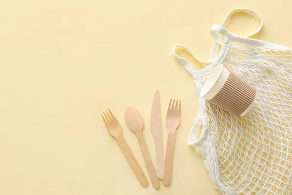 Wooden cutlery, paper cup and string bag on yellow background