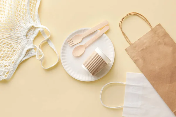 Eco tableware, string and paper bags on yellow background