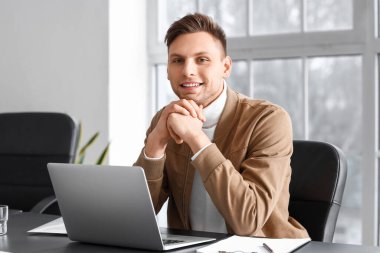 Ofiste dizüstü bilgisayarla çalışan gülümseyen iş adamı.