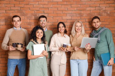 Dizüstü bilgisayarlı iş arkadaşları, kahve fincanları ve tuğla arka planda belgeler.