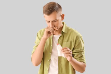 Young man with nosebleed and tissue on white background
