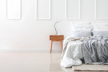 Ağaç dallı vazo, masada kahve fincanı ve ışık duvarının yanında rahat bir yatak.