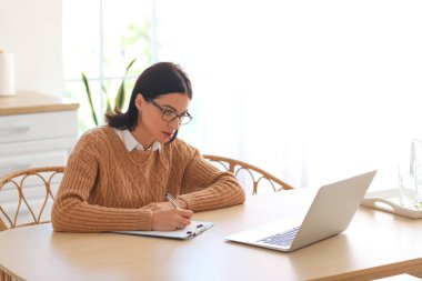 Kadın psikolog mutfakta hastayla görüntülü sohbet ediyor.