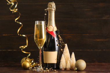 Şişe, bir kadeh şampanya ve ahşap arka planda Noel süsleri.