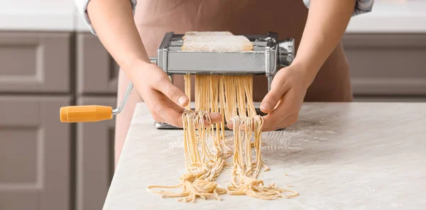 Woman using machine for making pasta in kitchen, closeup