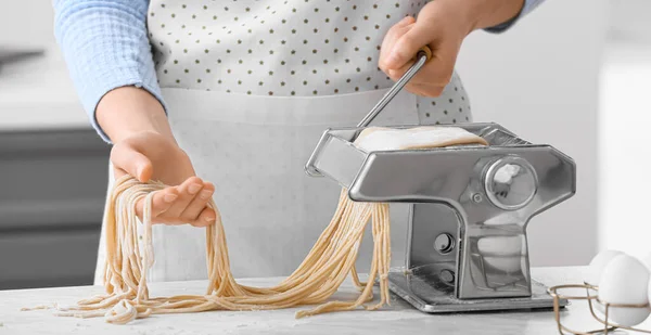 Woman making pasta with machine in kitchen, closeup