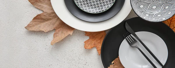 Plates with cutlery and autumn leaves on light background