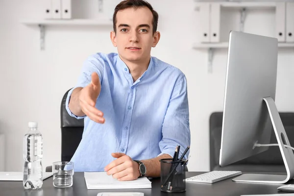Young businessman reaching out for handshake at table in office