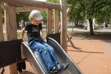 Bir ilkokul çocuğu oyun alanında oynuyor. Çocuk bir çocuk kaydırağına oturuyor..