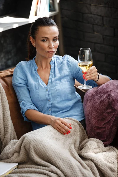 余暇の概念。幸せな美しい女性はソファの上に座ってガラスから白ワインを飲む屋内。女性過ごす彼女の自由日とリラックスで自宅一人で. — ストック写真
