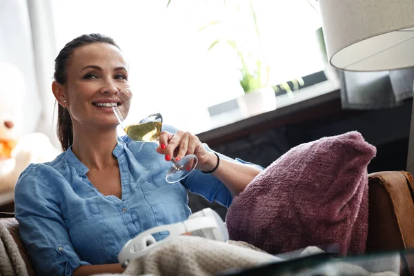 Boş zaman konsepti. Mutlu güzel kadın, kapalı bir koltukta otururken camdan beyaz şarap içer. Kadın boş gününü evde yalnız geçirir.. — Stok fotoğraf