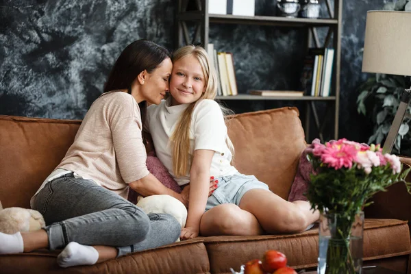 Mutter-Tochter-Beziehung. Eine Frau und ein Mädchen im Teenageralter sitzen vor dem Fernseher auf der Couch und unterhalten sich. Die Familie verbringt Zeit zu Hause. Kleiner Hund liegt auf Schoß — Stockfoto